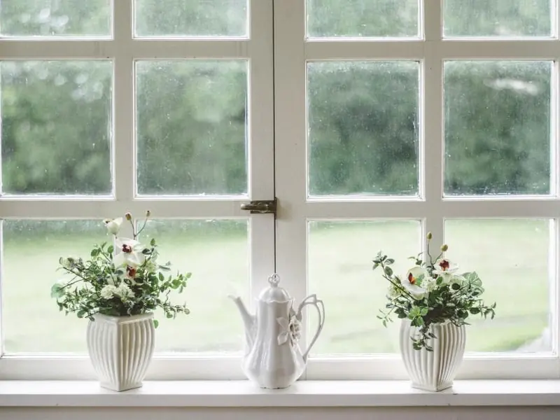 Janela de caixilho branco com vasos de flores e um bule no peitoril